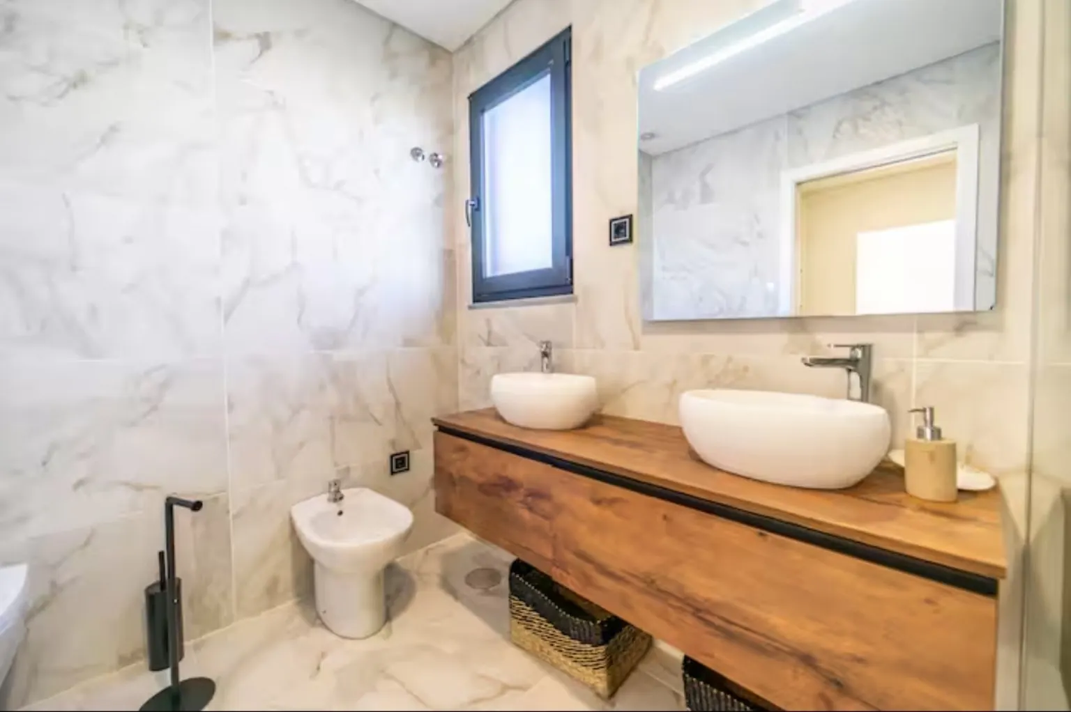Baño de mármol blanco con mueble de madera flotante y lavabo de cerámica sobre encimera