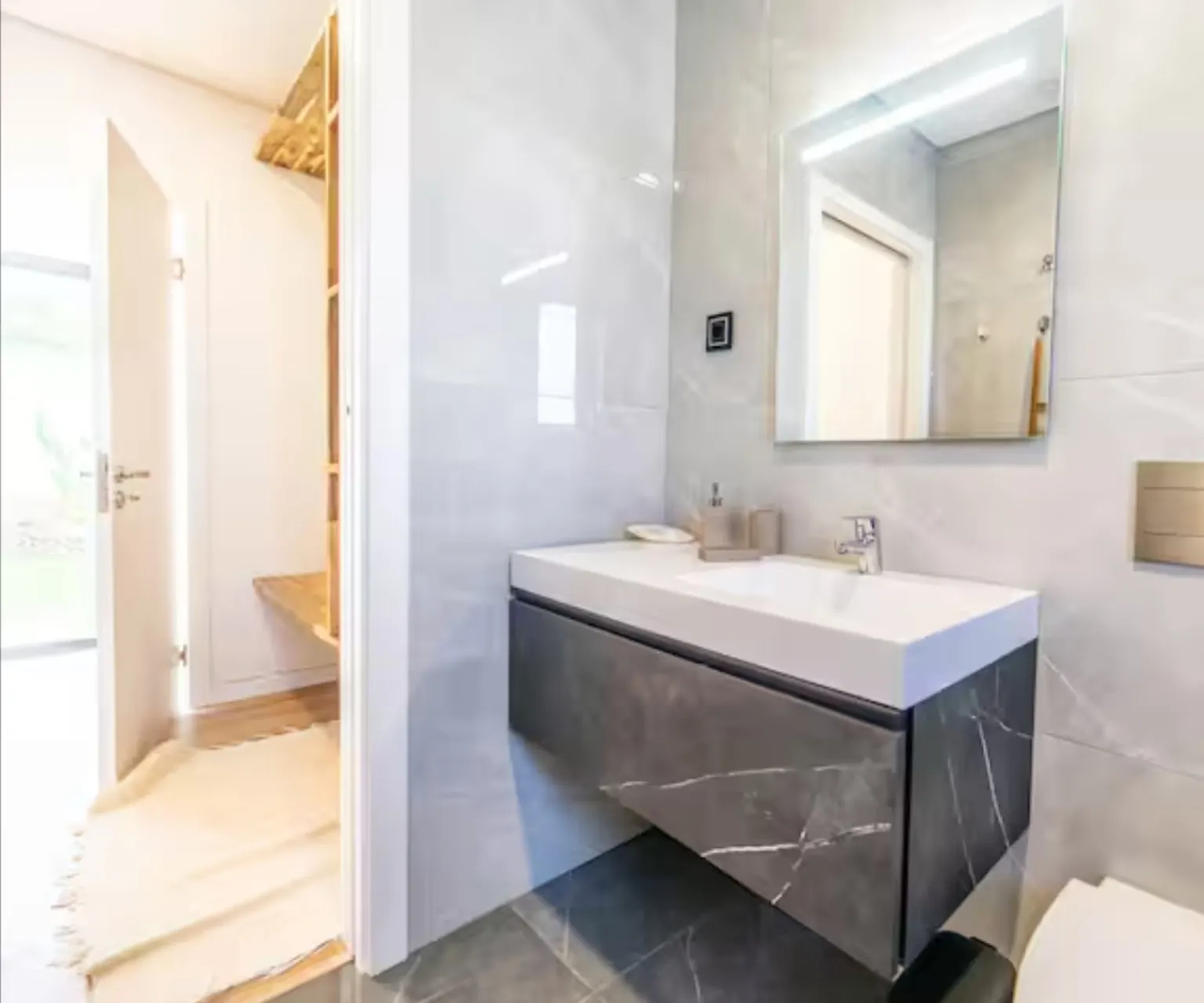 Baño con mueble de lavabo en efecto mármol gris y espejo retroiluminado