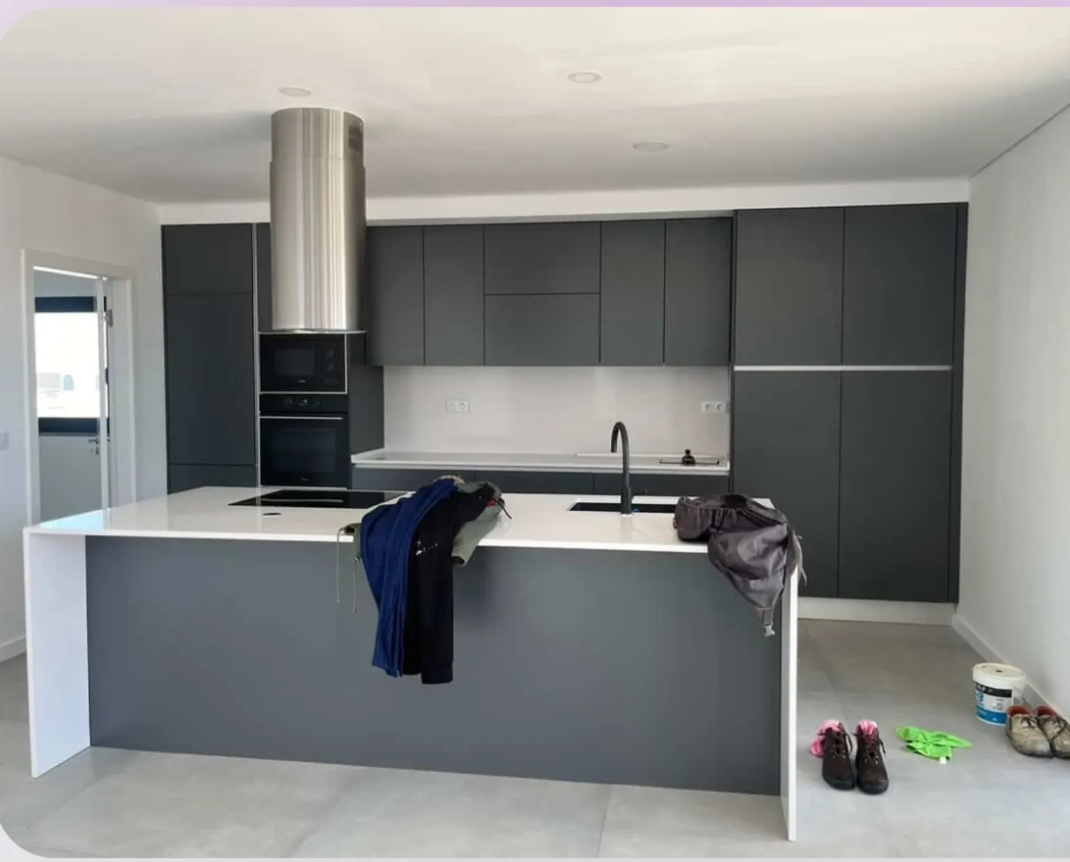 Cocina gris con isla blanca antes de la reforma, con ropa y objetos sobre la encimera