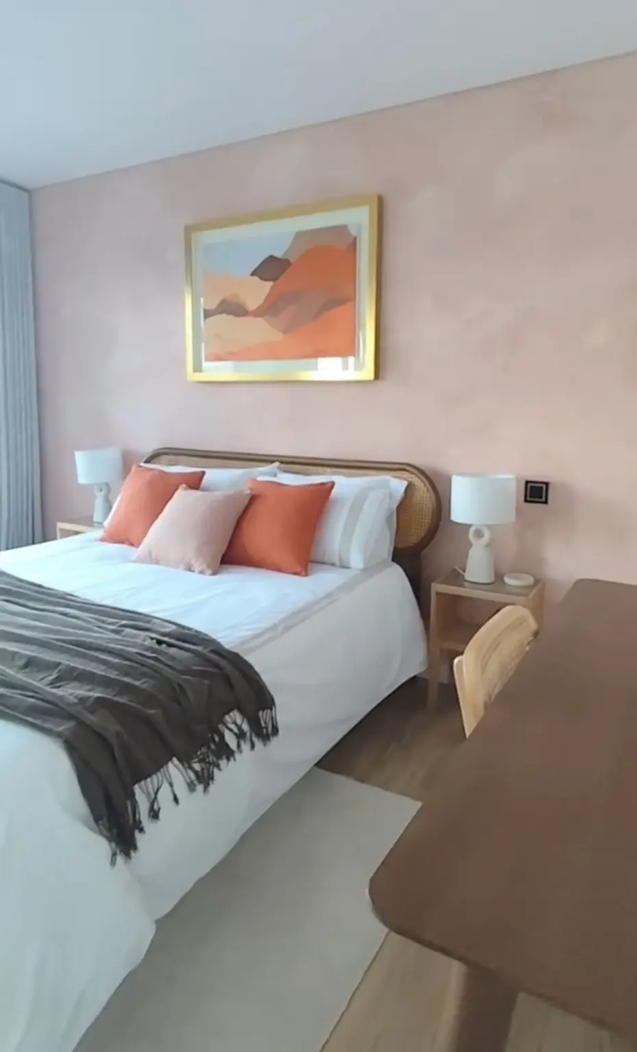 Dormitorio con pared rosada, cojines naranjas y un cuadro de paisaje sobre la cama