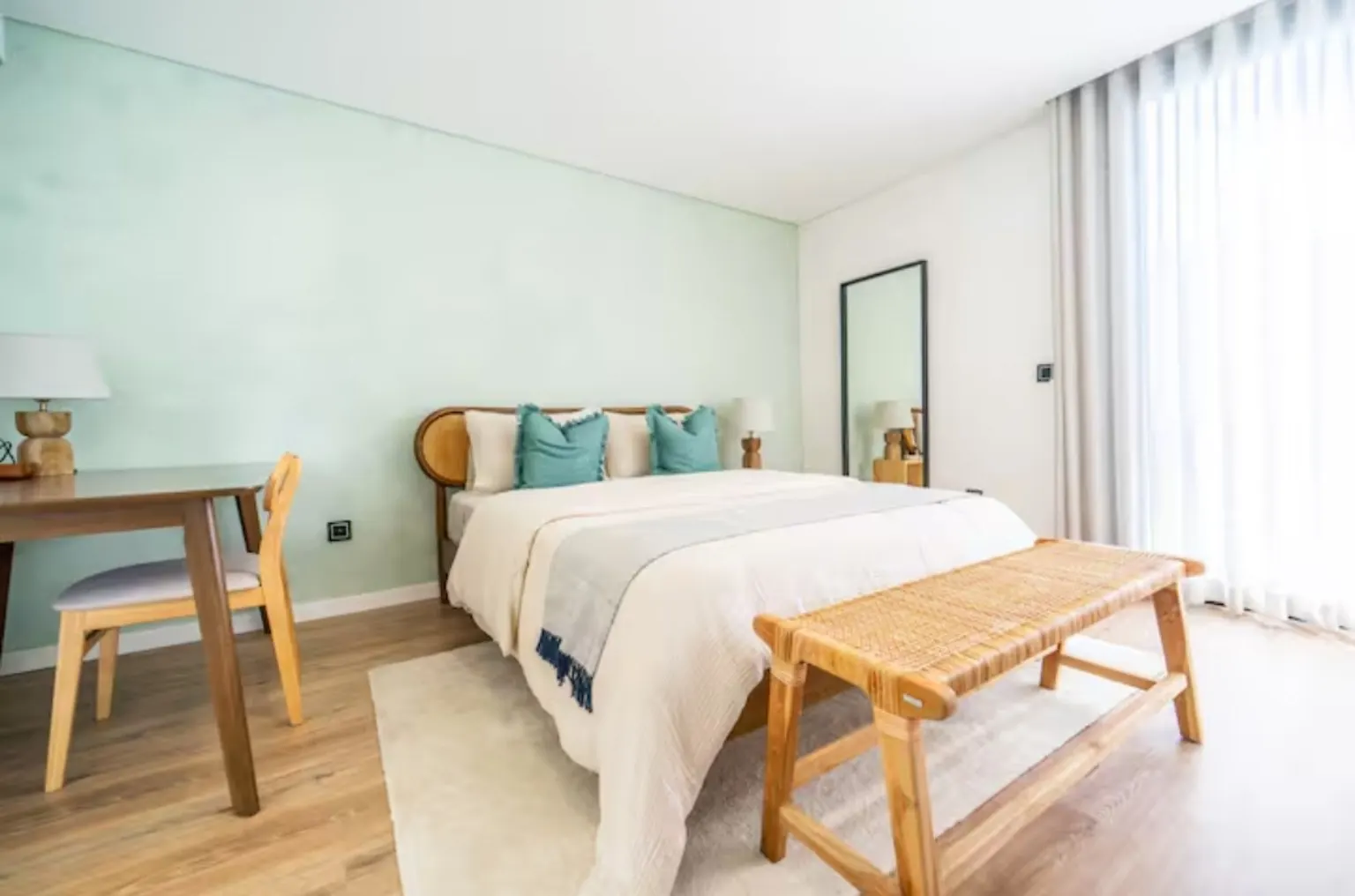 Dormitorio con pared verde menta, cabecero de ratán, banco de madera y alfombra de fibra