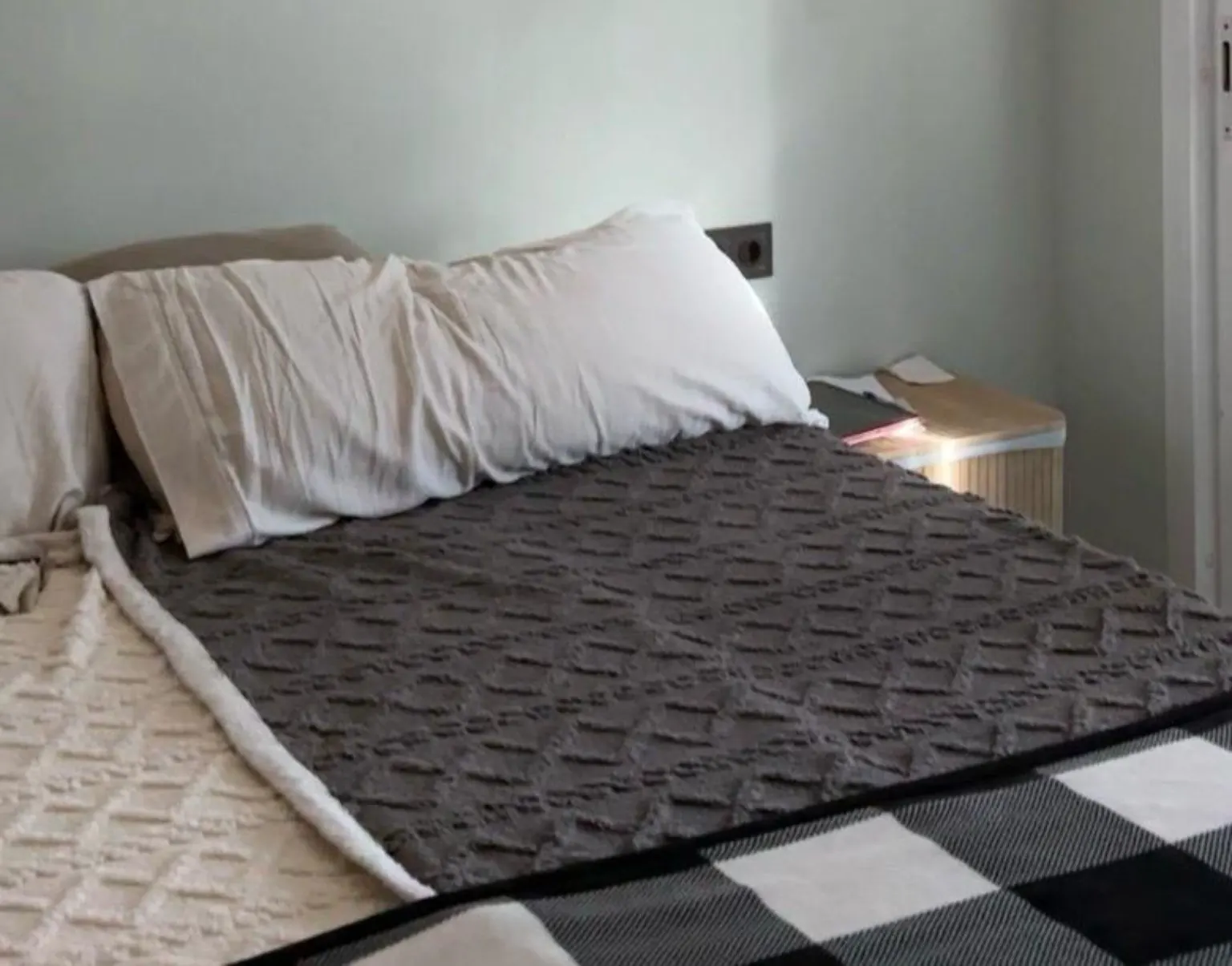 Cama vestida con colcha gris texturizada y manta de cuadros blancos y negros