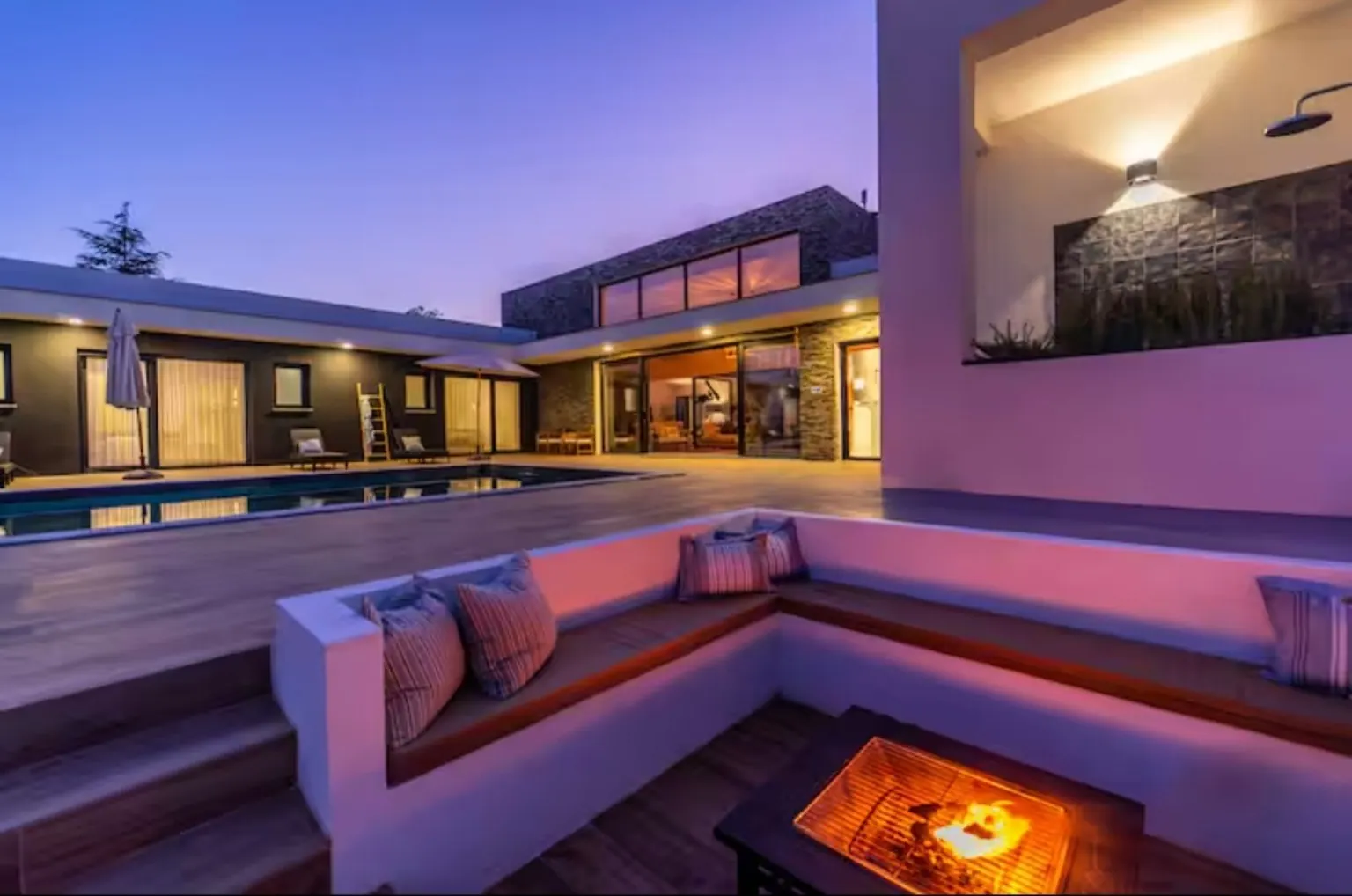 Zona de estar exterior con sofá de obra y brasero encendido al anochecer