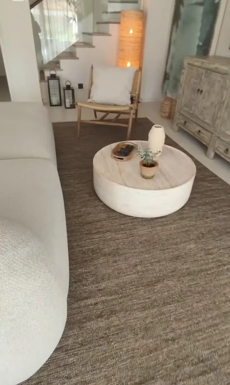 Rincón de salón con sofá curvo blanco, alfombra de yute y mesa de centro redonda