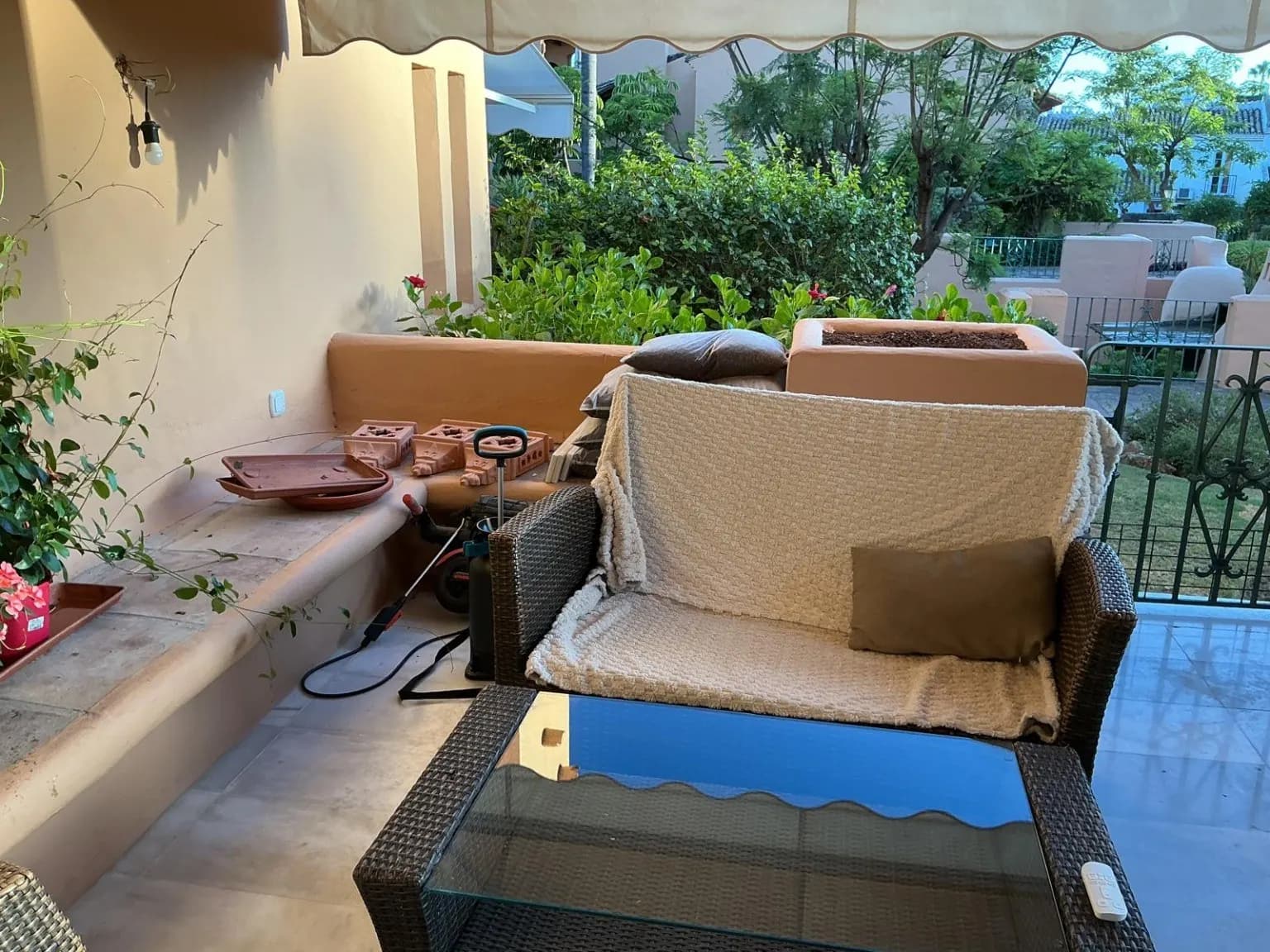 Terraza con butaca tapizada, mesa de cristal y jardín al fondo