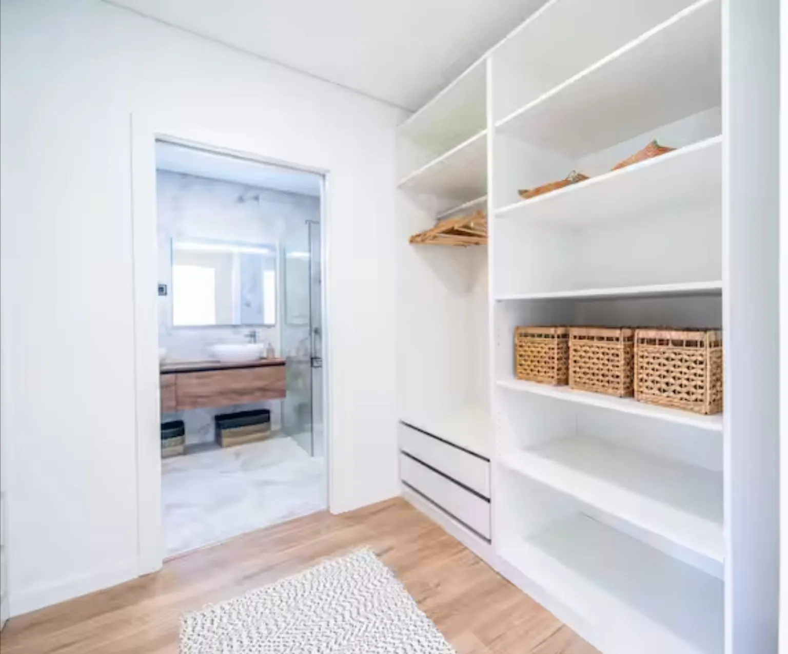 Vestidor abierto blanco con estantes, cajones y cestas de fibra junto al baño